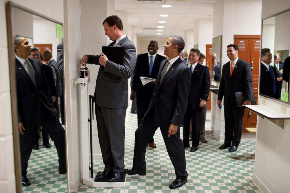 A photograph used as an example of understanding beyond the comprehension of an AI program: President Obama surreptitiously adds a few pounds as a colleague weighs himself. (Credit: Official White House photo by Pete Souza)